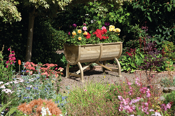 a half barrel wooden planter full of colourful plants sitting in a pretty garden