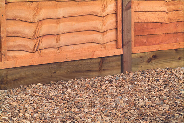 a close up of a wooden gravel board under an overlap fence and sitting on a bed of gravel