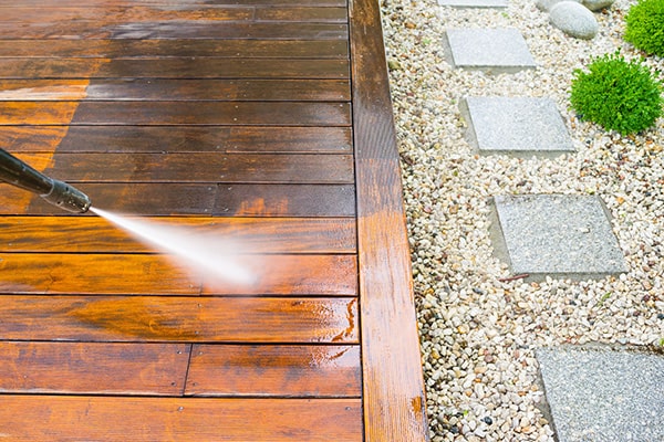a person pressure washing a wooden decked path