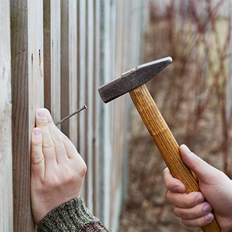man installing fence on driveway with a hammer
