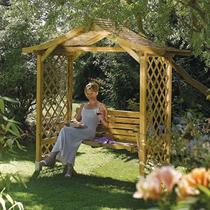 A woman in a white dress sat on the Rowlinson Dartmouth Wooden Swing Seat.