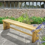 The Forest Double Sleeper Wooden Garden Bench, situated on a patio, with shrubs and an outhouse in the background.