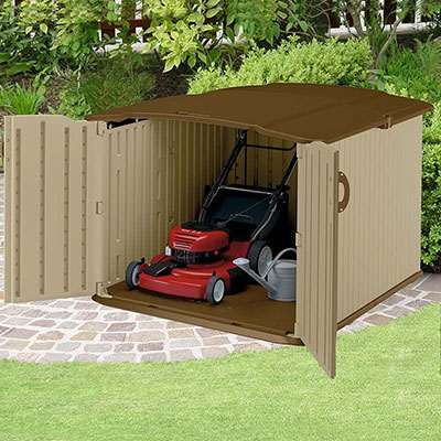 A brown, plastic lawn mower storage shed containing a red lawn mower